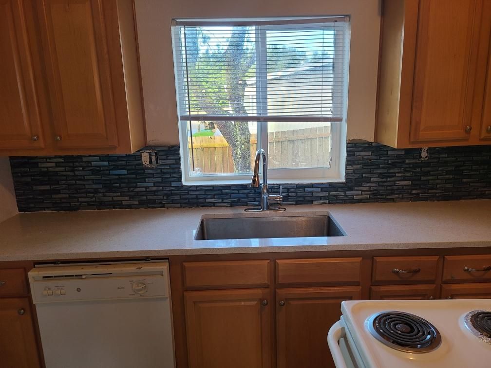 Kitchen with window above sink, wood cabinets, black tile backsplash, dishwasher, and electric stove.