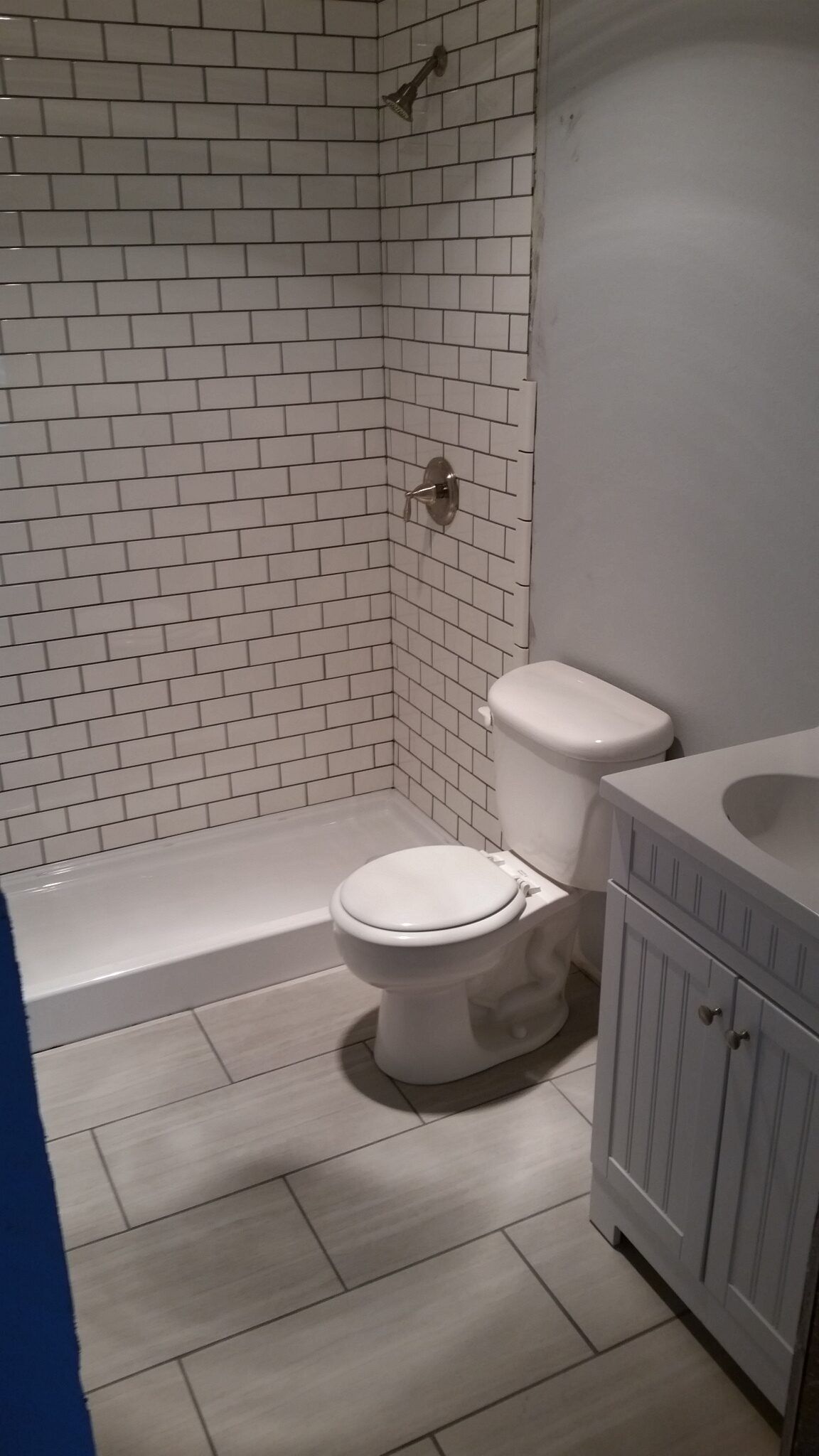 Small tiled bathroom with a toilet, bathtub, and white vanity cabinet.