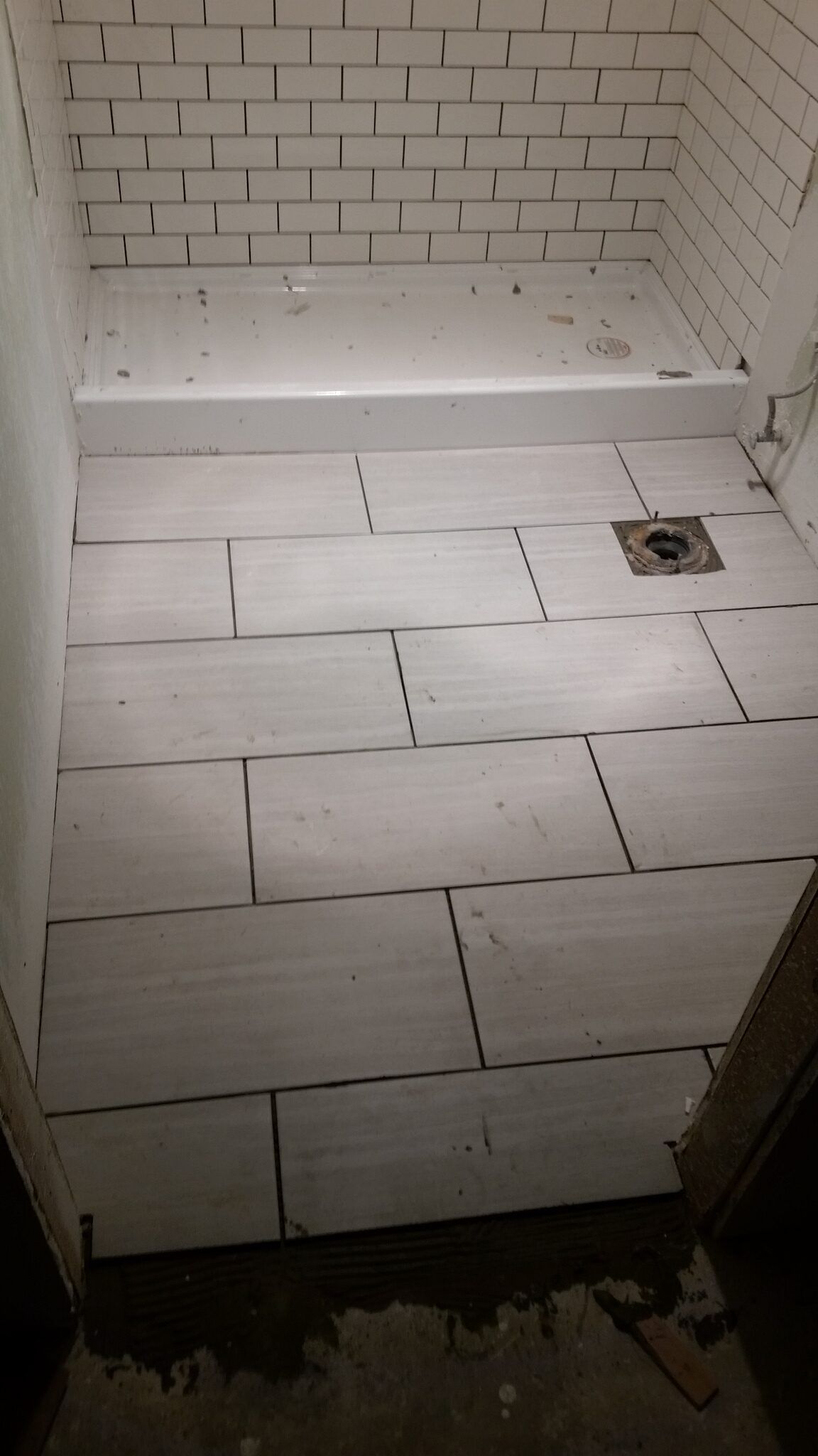 Tiled shower stall under construction with white wall tiles and a floor drain.