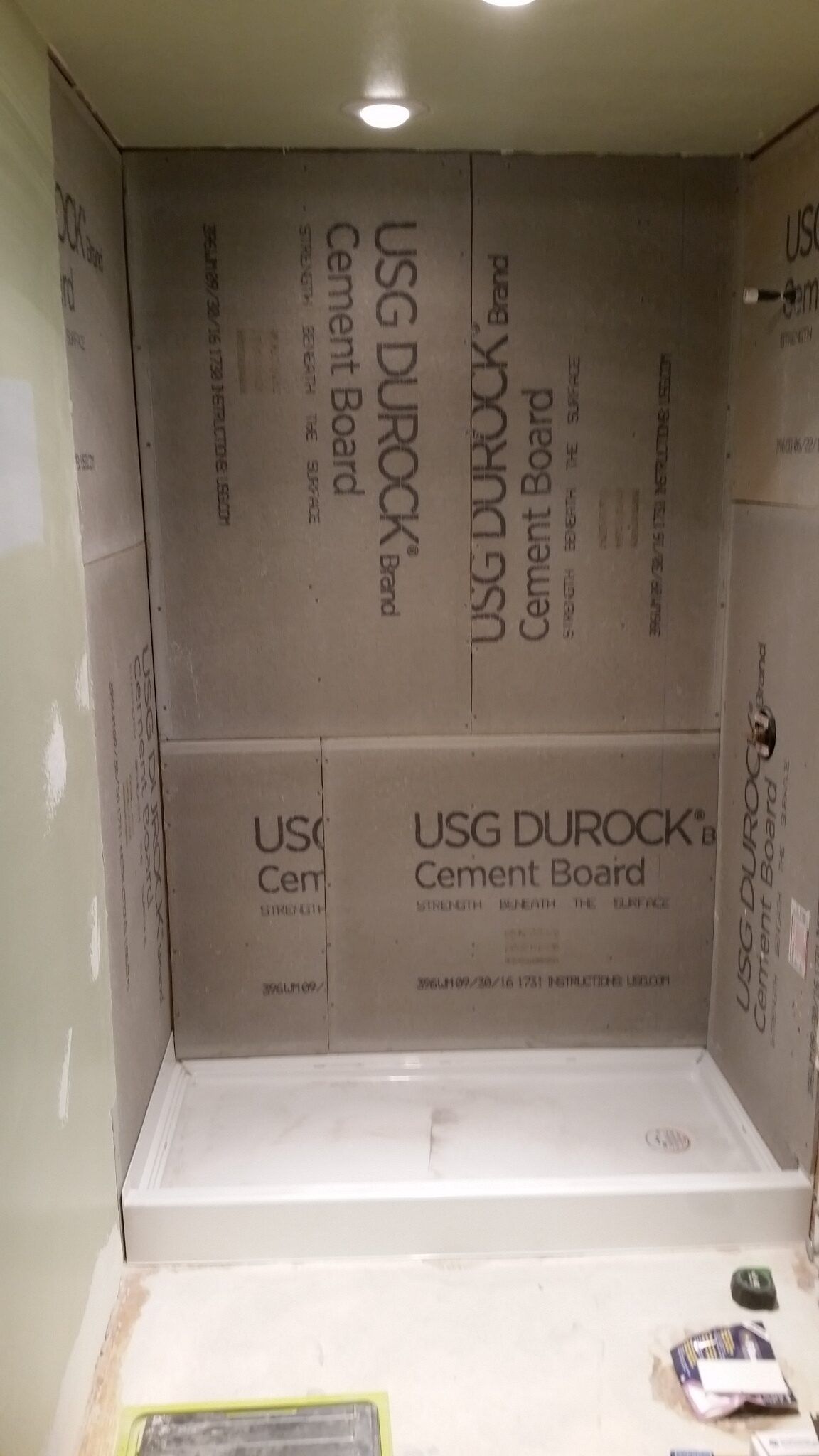 Small bathroom shower alcove lined with USG Durock cement board and a white shower base installed.