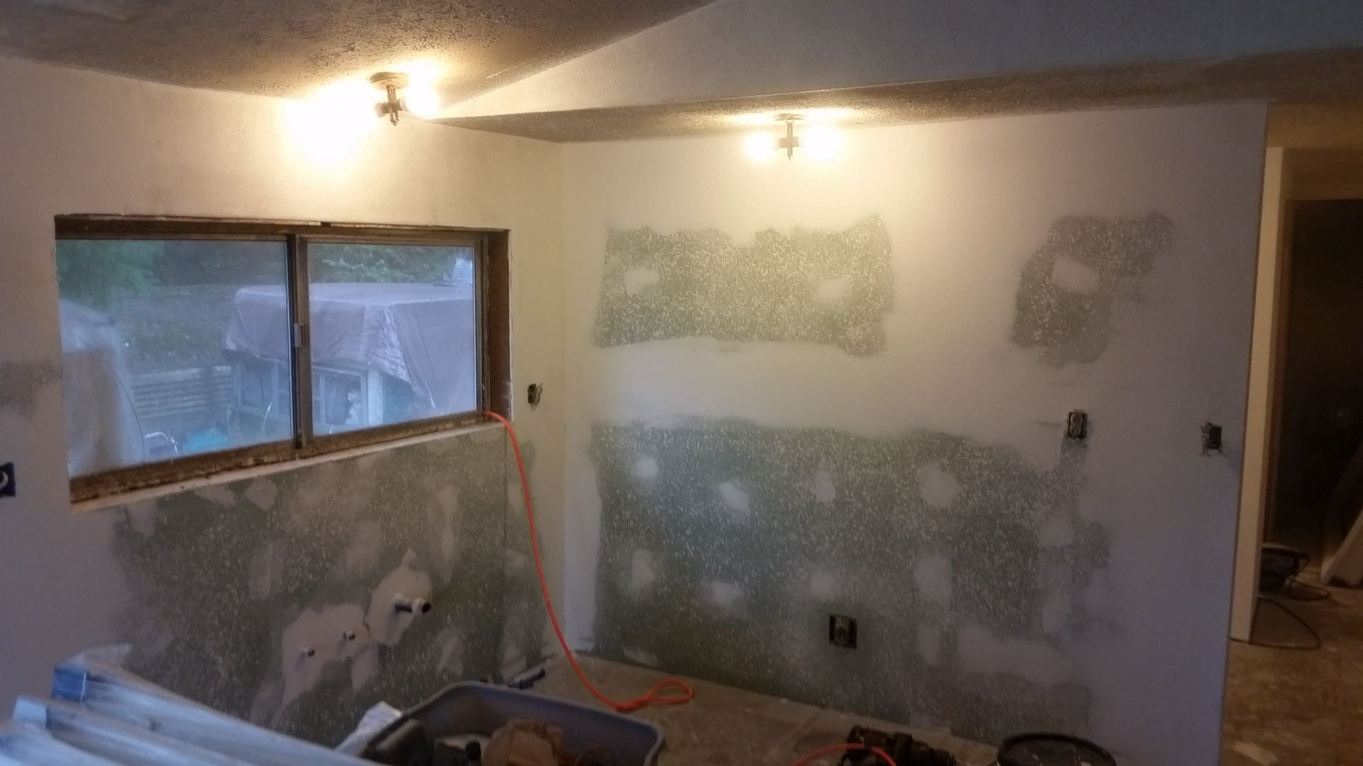 Partially renovated room with patchy drywall, a window, and a ceiling light on