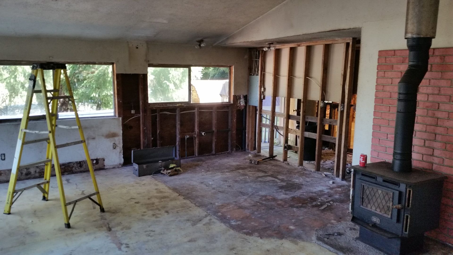 Partially demolished room with exposed studs, ladder, and wood stove during renovation