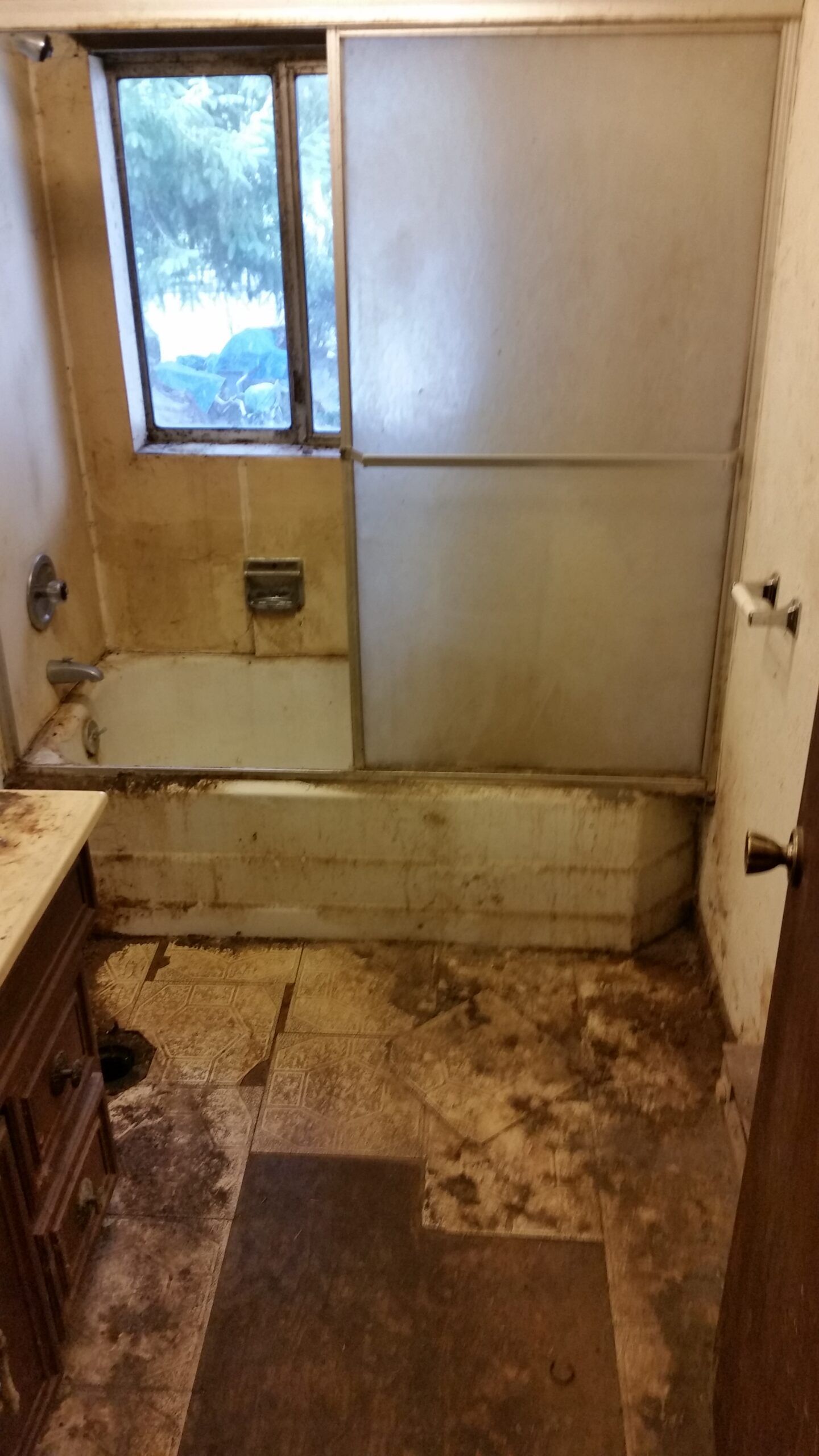 A small, dirty bathroom with a bathtub, window, and stained walls and floor