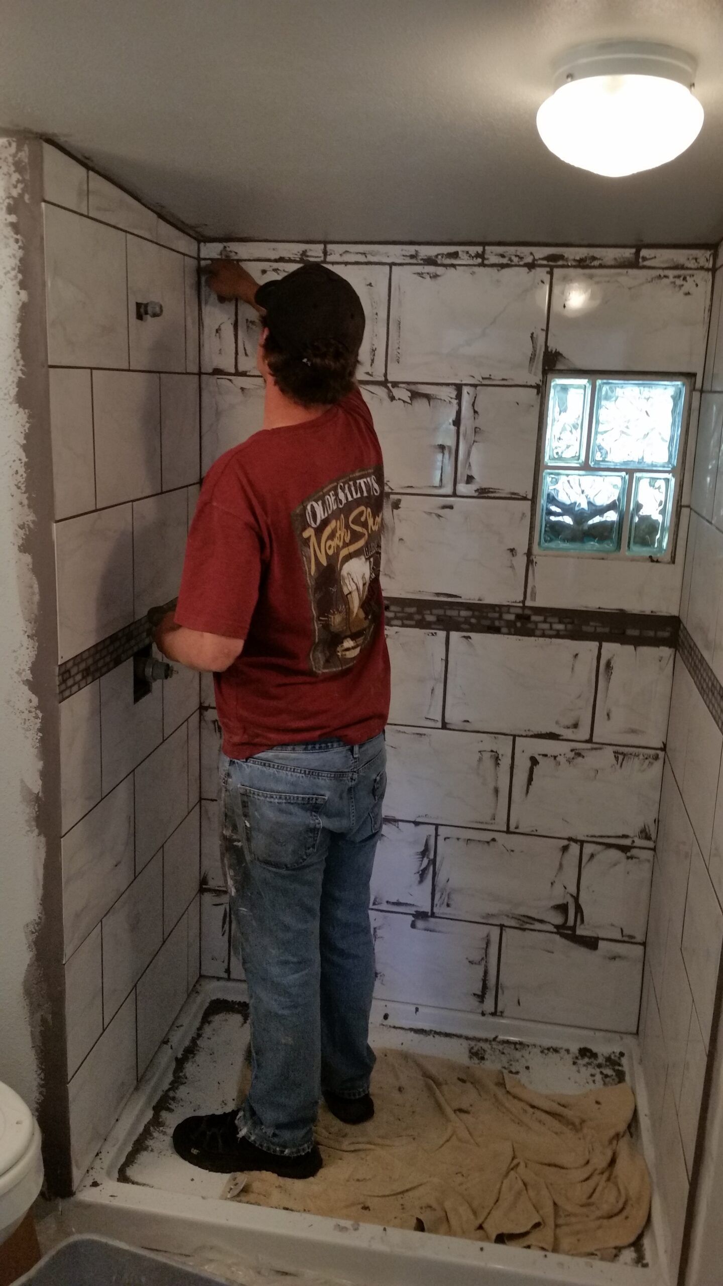 Person in a red shirt standing in a small unfinished room with cinderblock walls and a window.