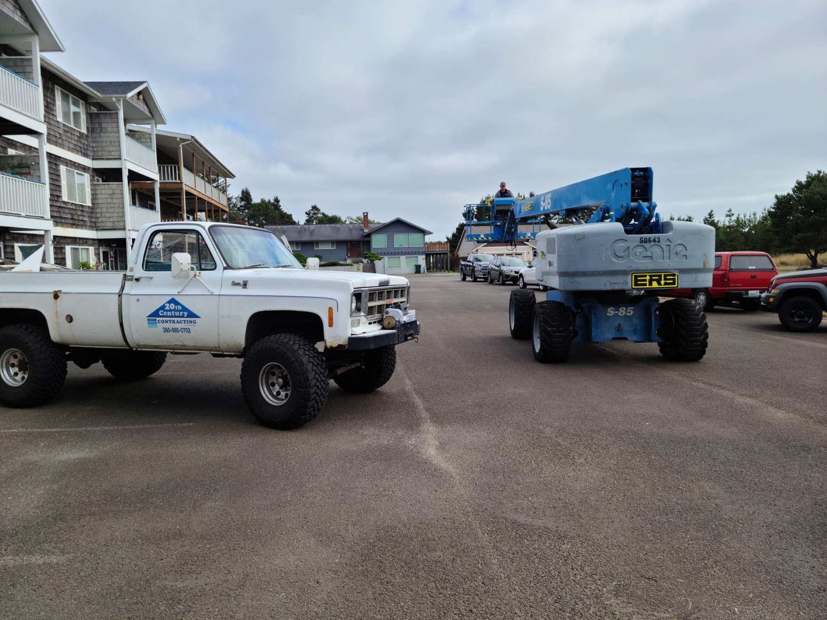 Two pickup trucks with utility lifts parked on a lot near waterfront buildings