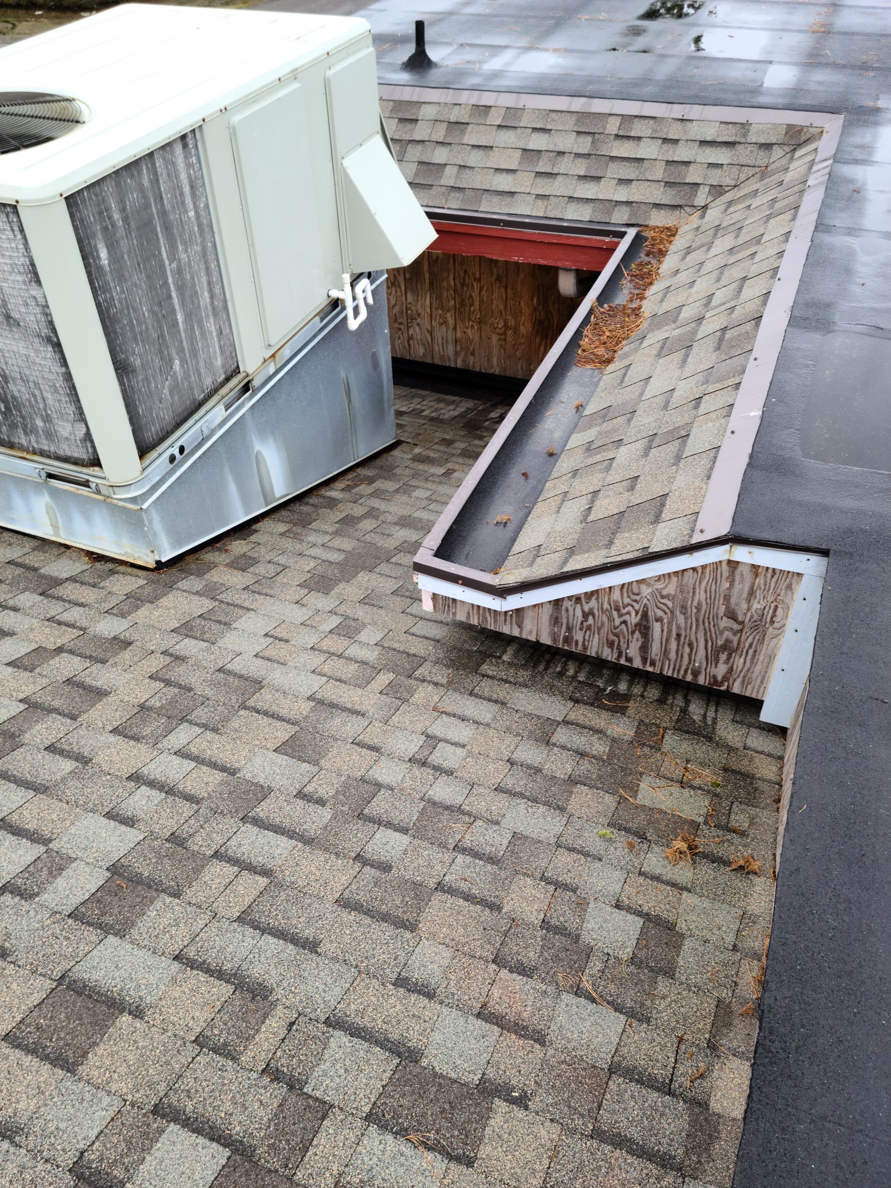 Rooftop HVAC unit beside a raised vent opening and gray shingle roof edging