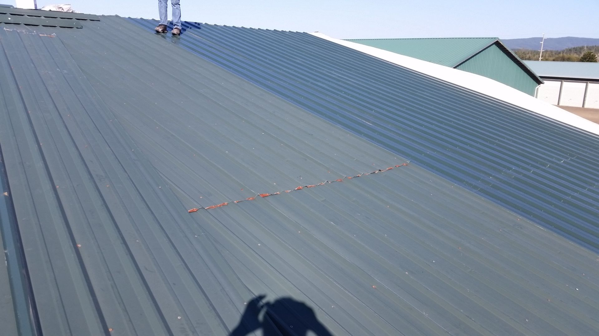 Corrugated gray metal roof with a small vent and distant rooftops under a clear sky