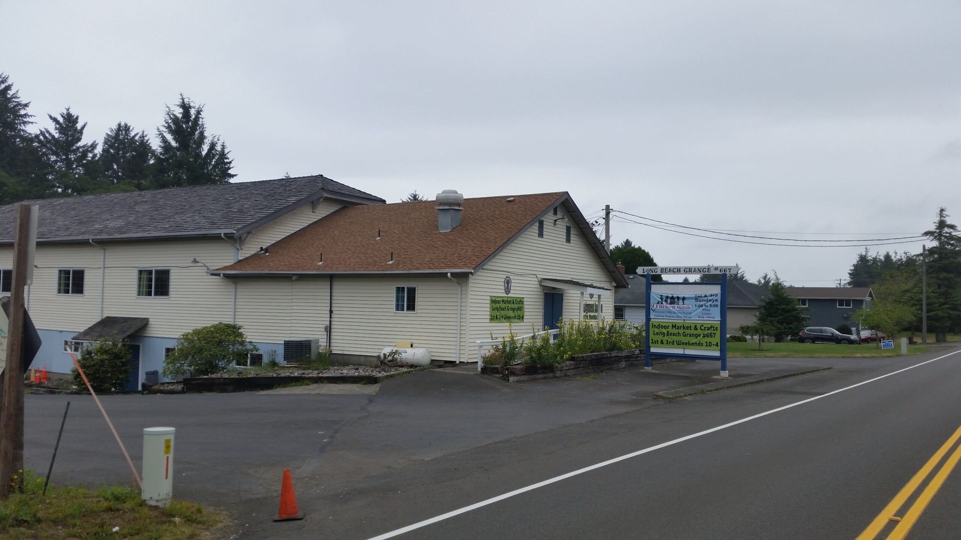 Roadside building with a signboard, orange cone, and empty wet street under cloudy skies.