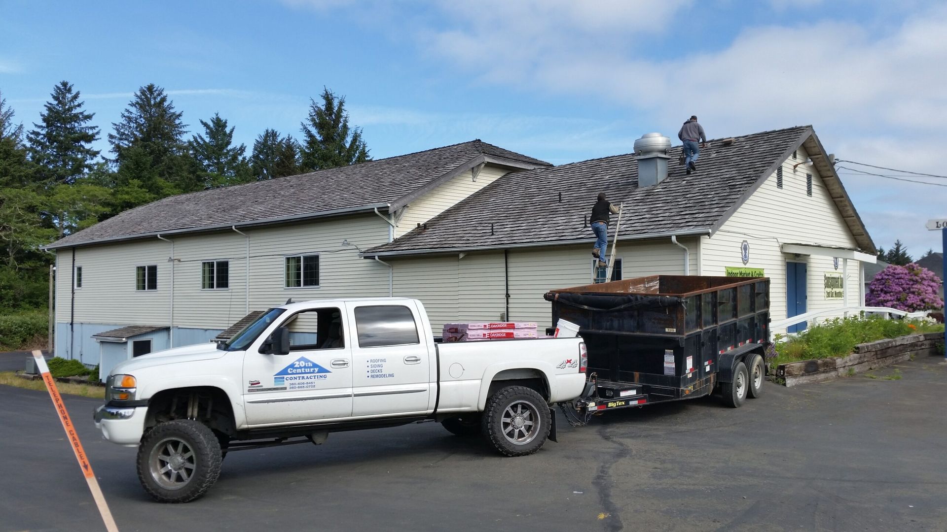 White pickup truck with dump trailer parked beside a white house on a driveway under a blue sky