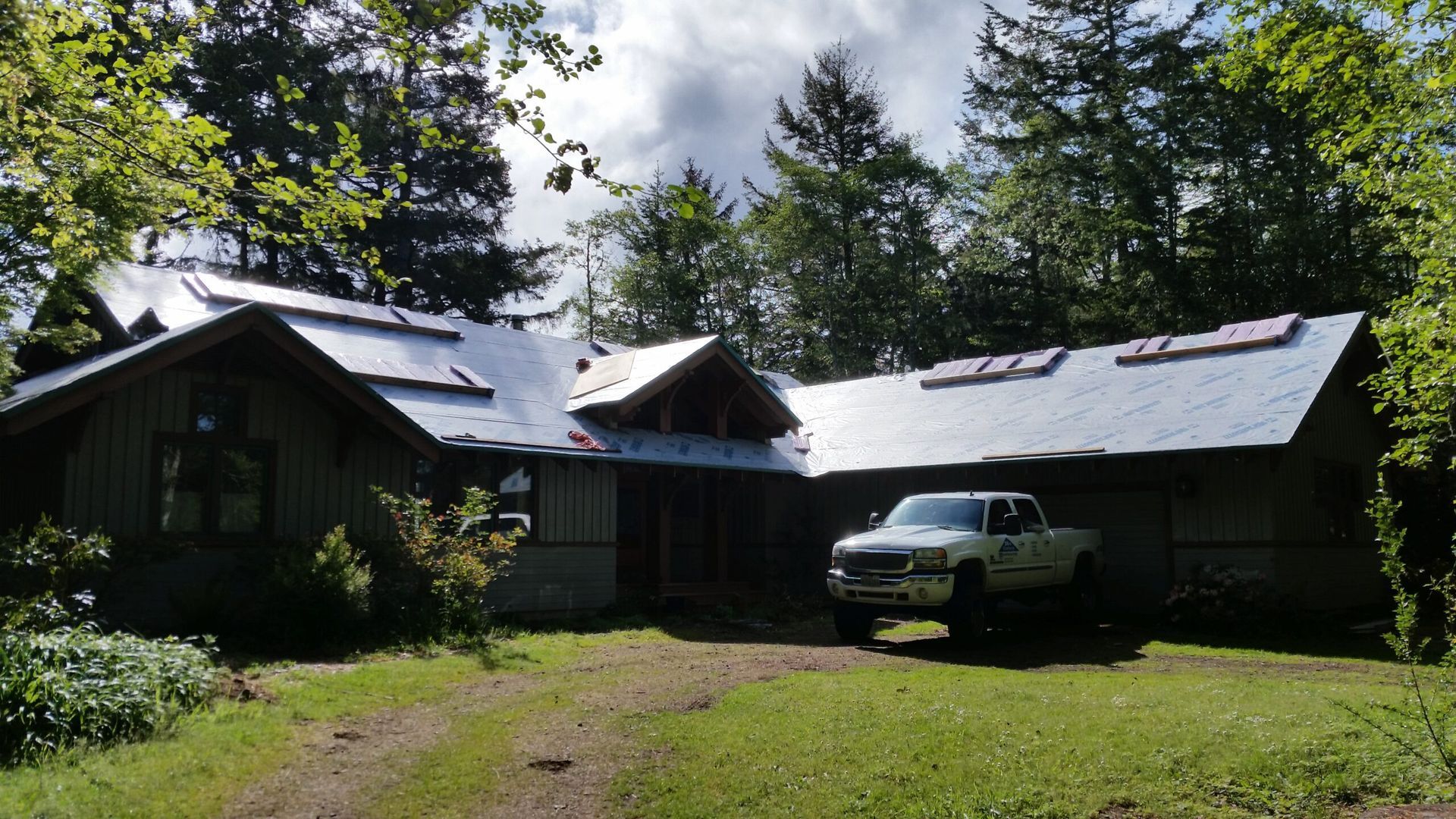 Rustic cabin with a silver SUV parked on a grassy driveway under trees