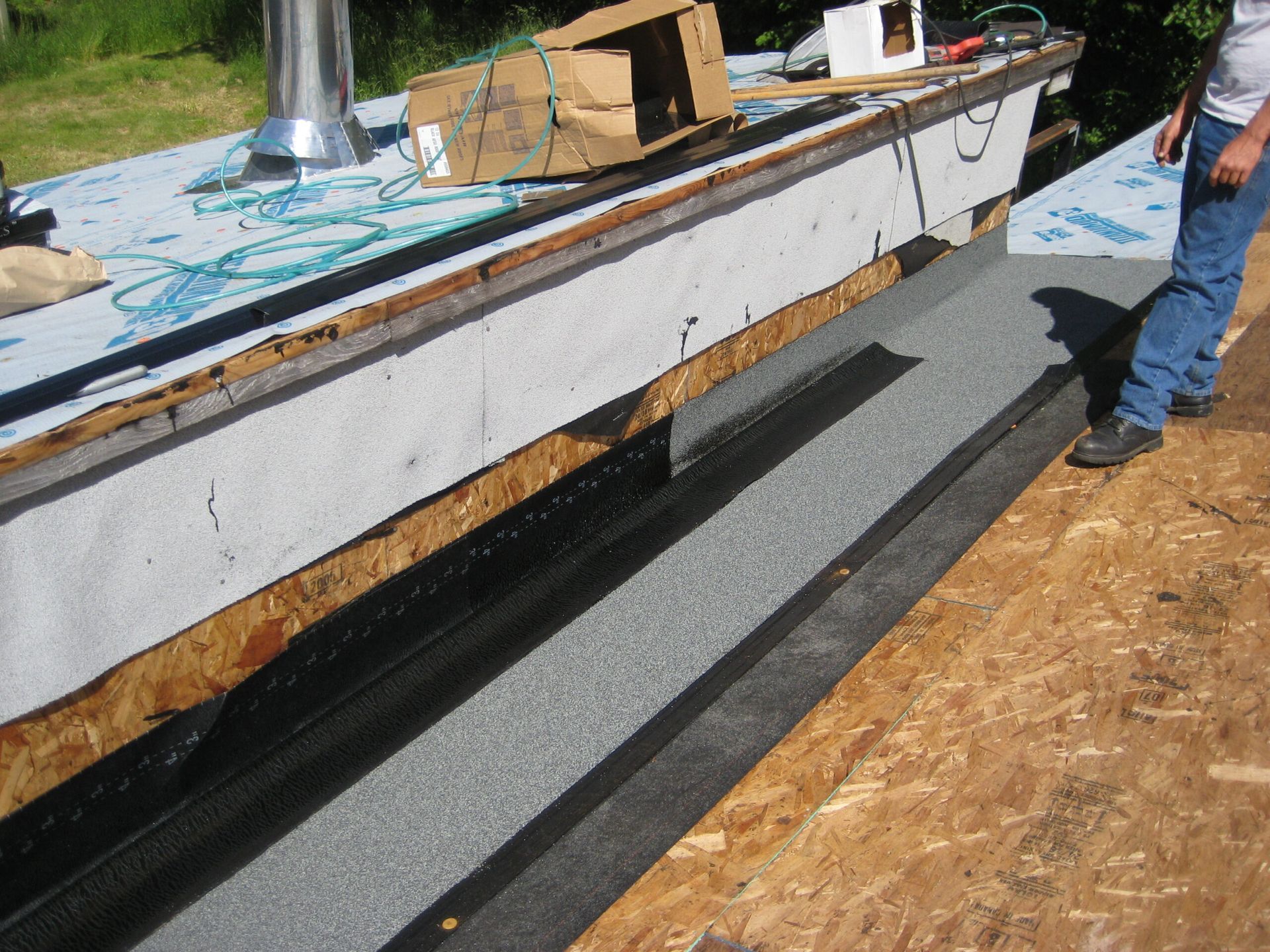 House roof under construction with workers installing a black metal roof strip along the edge
