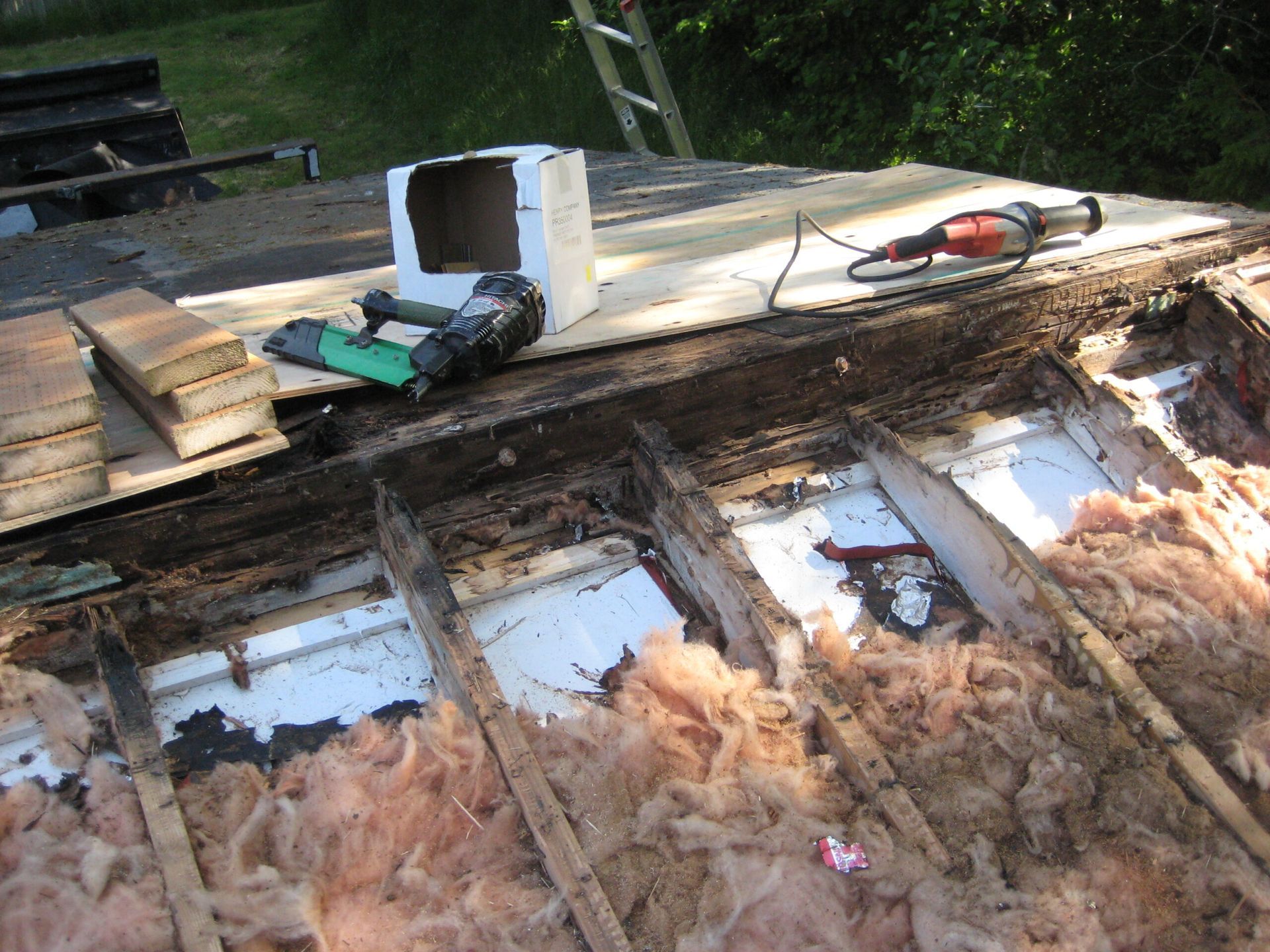 Roof repair with exposed wood, insulation, and tools on a partially stripped rooftop