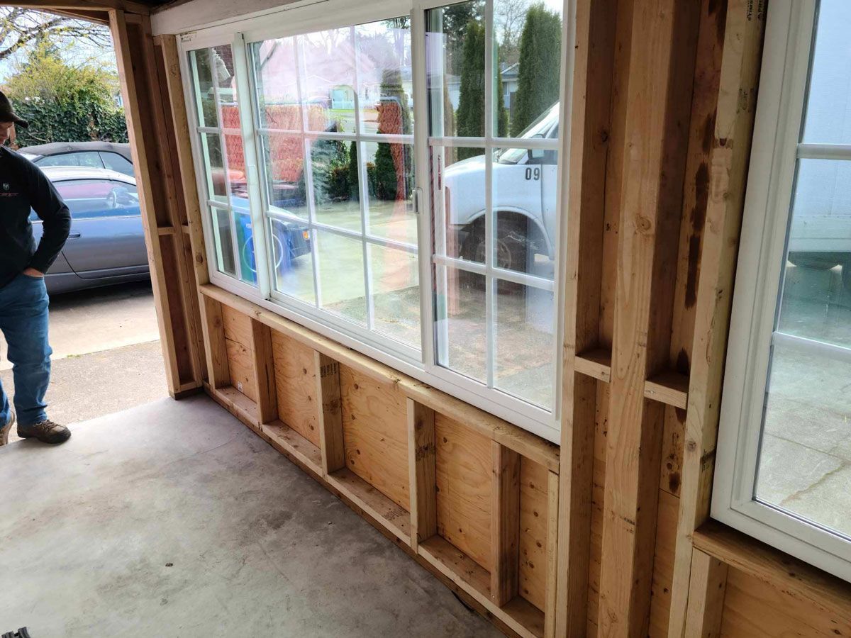 Interior under construction with exposed wood framing and large windows beside a sidewalk.