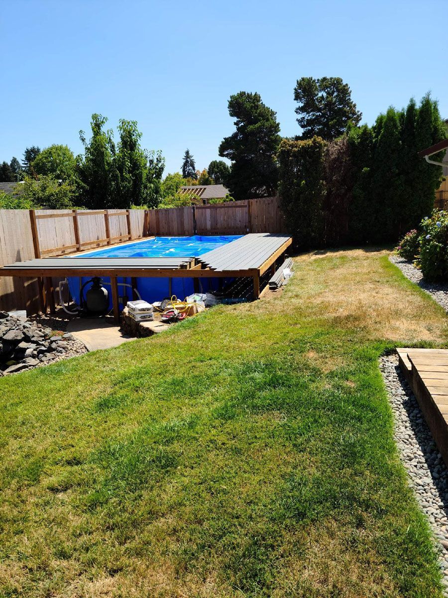Backyard with above-ground pool, green lawn, and trees under bright sunlight