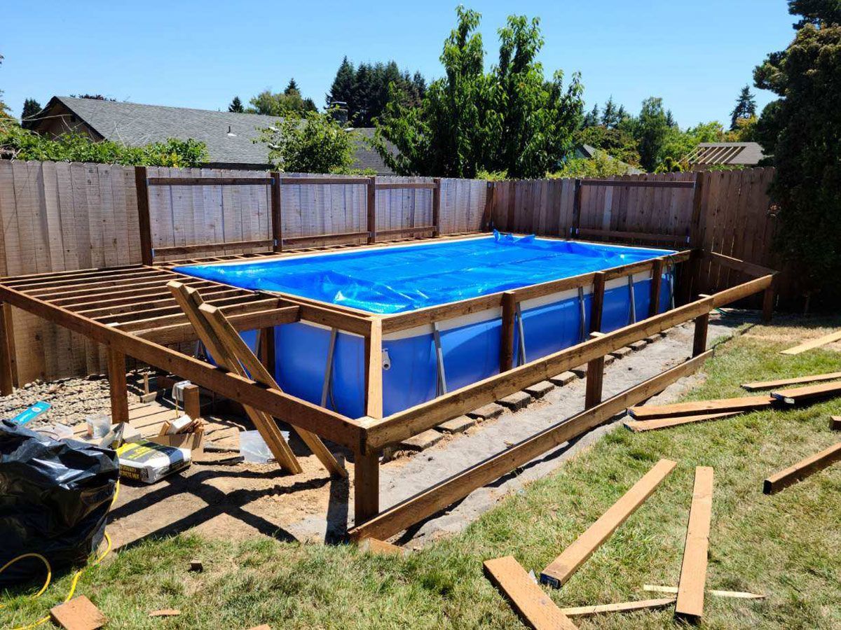 Backyard above-ground pool with blue liner, wooden frame, and fencing under construction