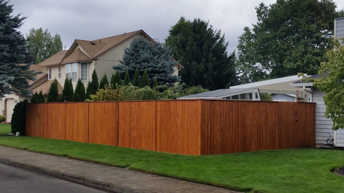 Wooden privacy fence along a grassy suburban street, with houses and trees behind it