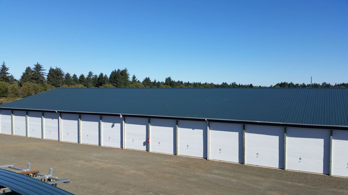 Long white storage building with a dark blue roof on a dry lot under a clear sky