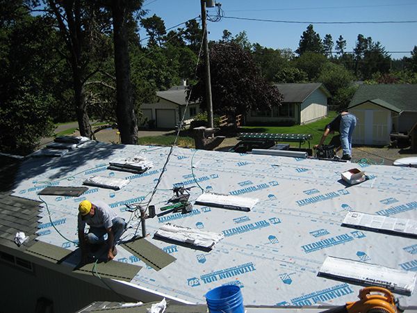 Workers installing roofing on a house with white underlayment and scattered materials on a sunny day