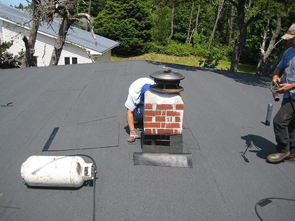 Workers installing a rooftop vent on a flat roof, with tools and a white tank nearby