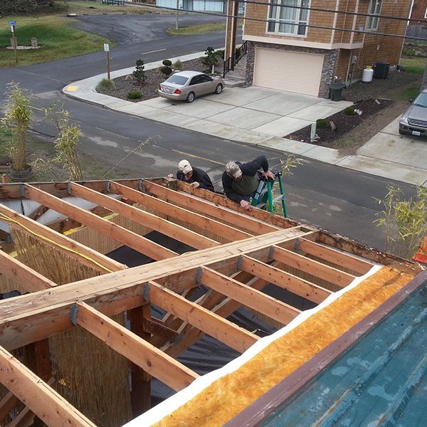 Workers repairing roof framing on a house, with lumber exposed and a ladder on the roof.