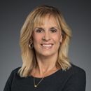 Devra smiling with blonde hair in a black top on a gray background