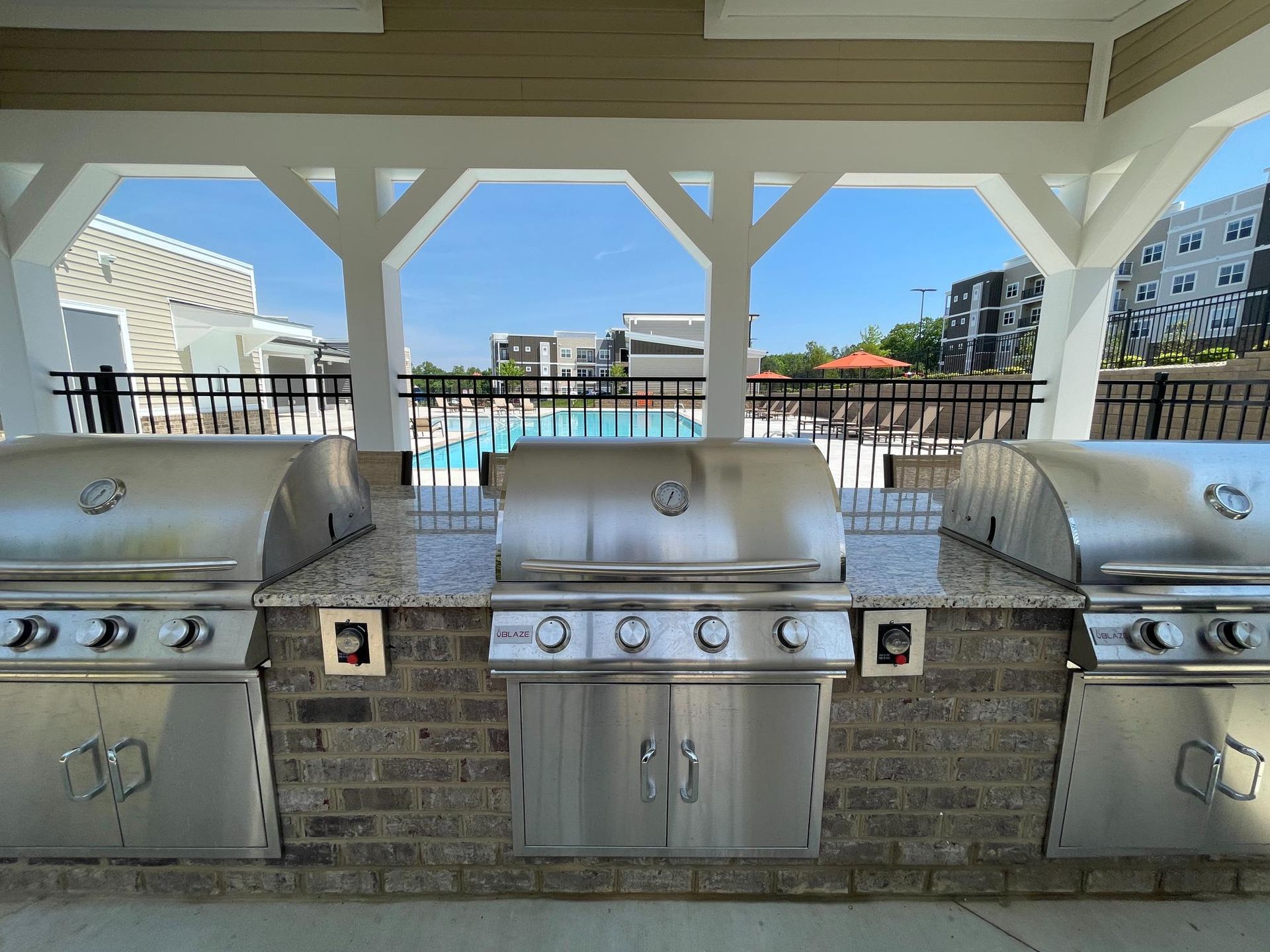 A stainless steel grill is sitting under a canopy overlooking a pool.