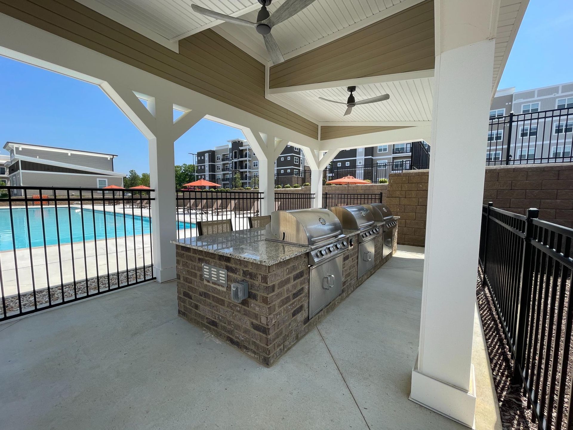 A patio with a grill and a pool in the background.