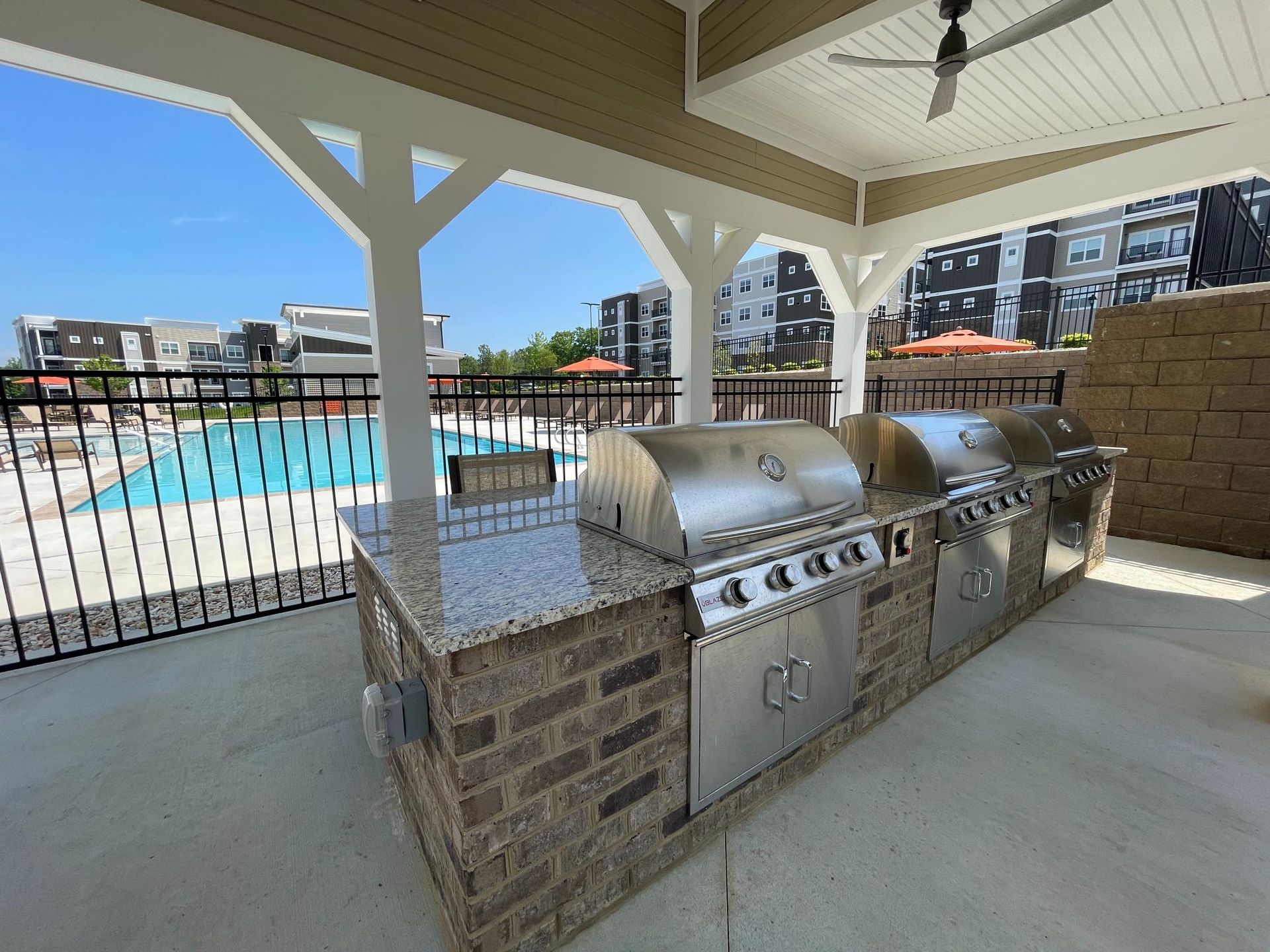 A large outdoor kitchen with a grill and a pool in the background.