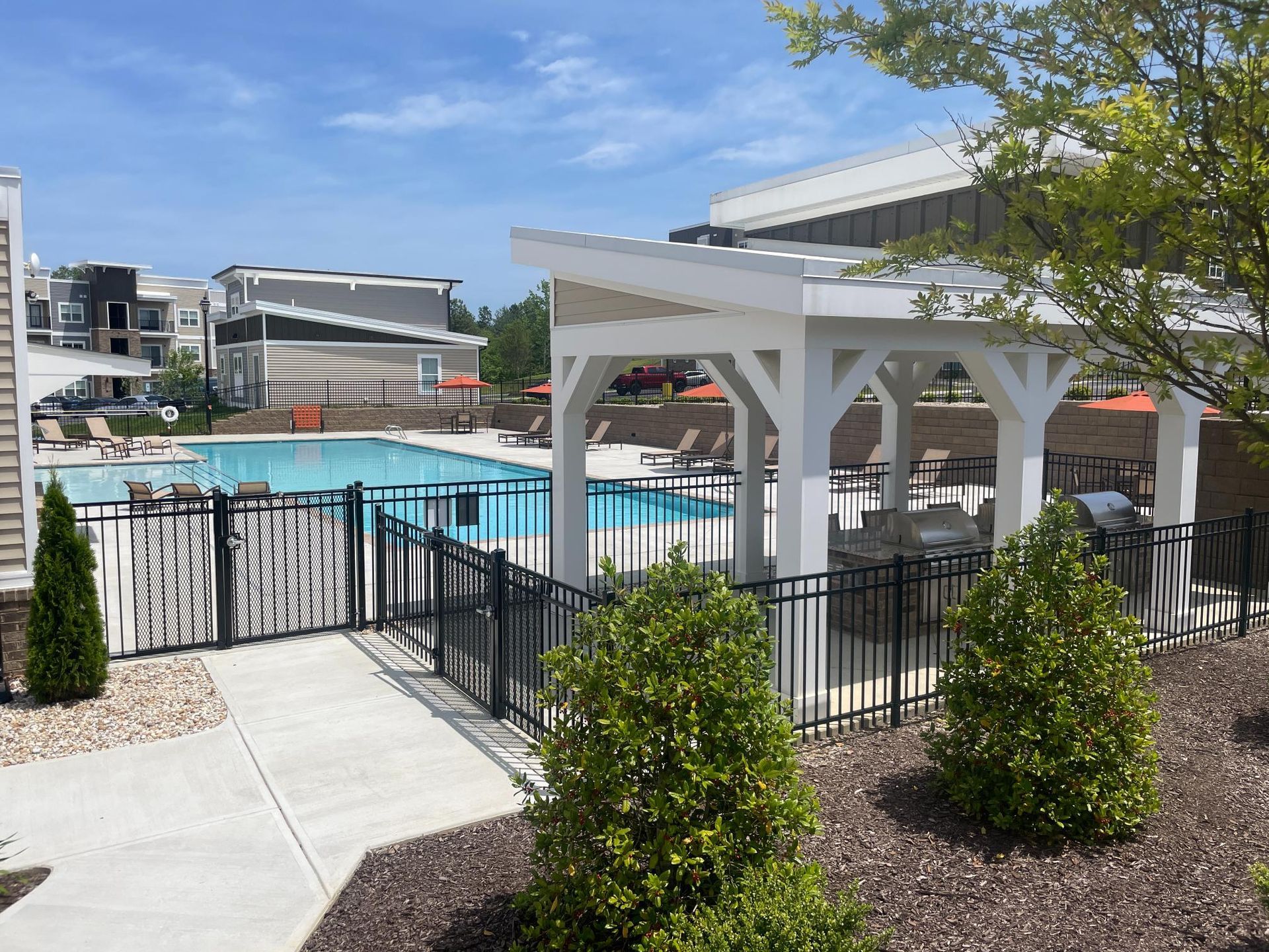 A large swimming pool is surrounded by a fence and a pergola.