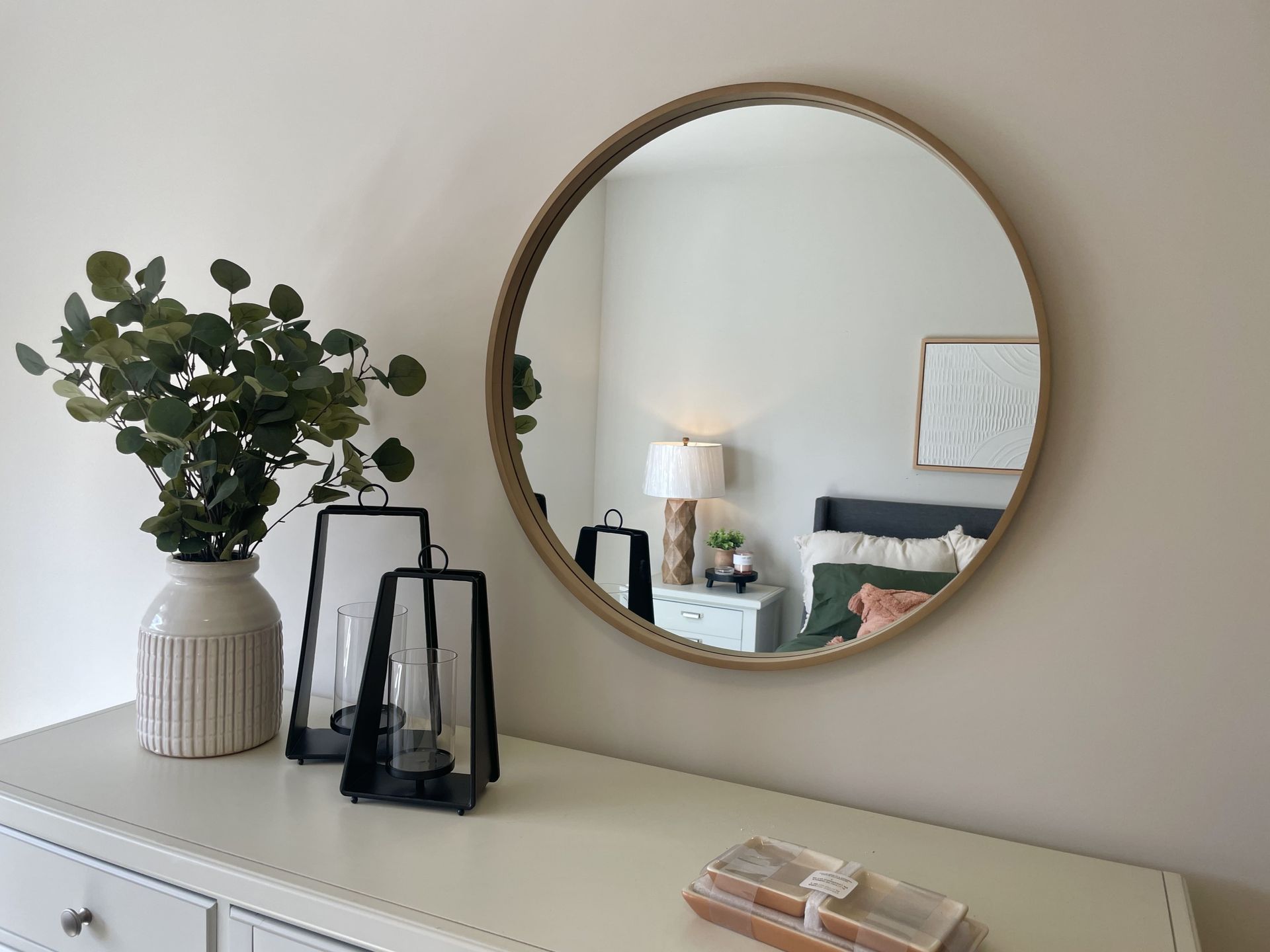 A round mirror is hanging on a wall above a dresser in a bedroom.