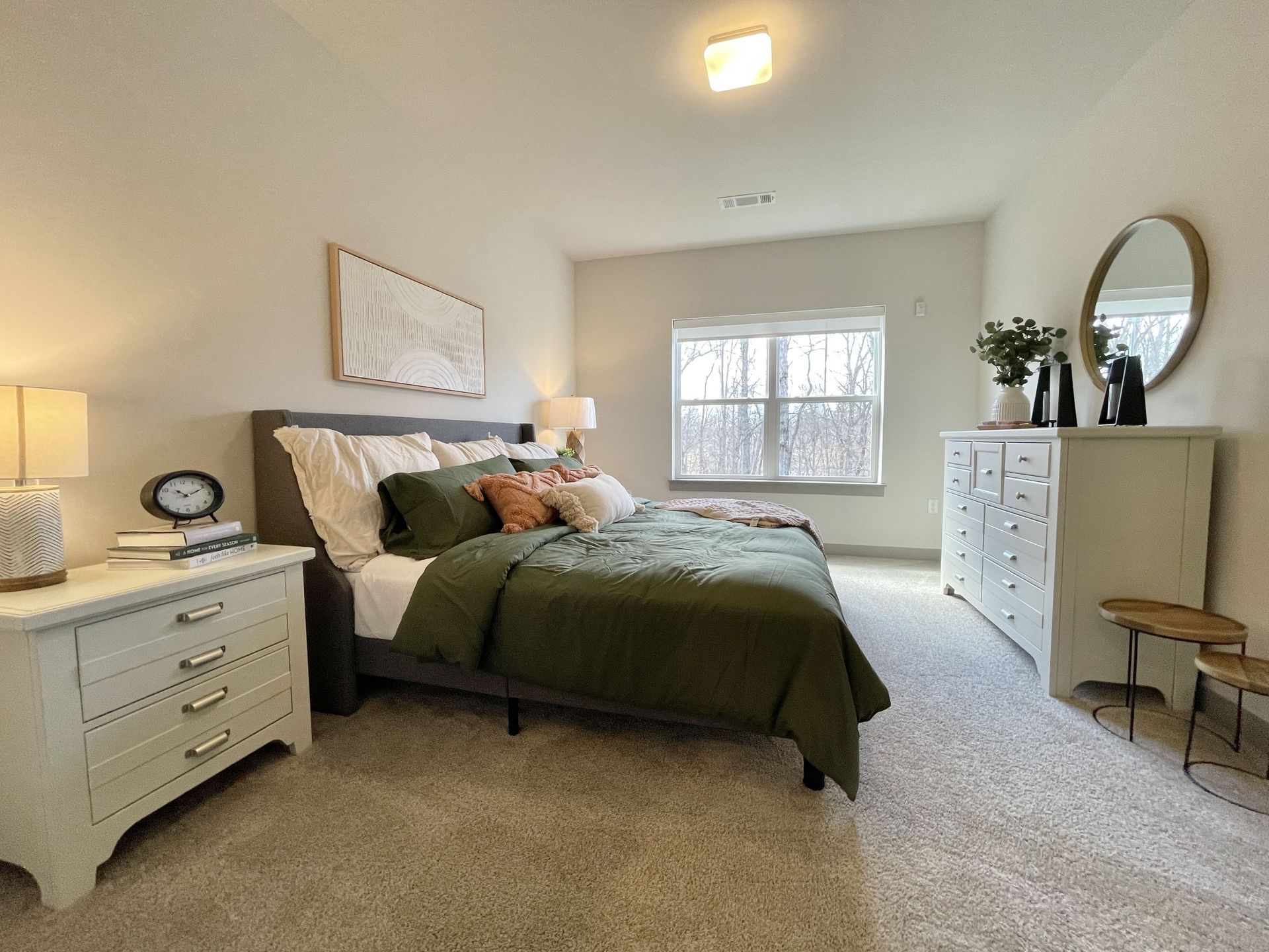 A bedroom with a bed , dresser , nightstand and mirror.