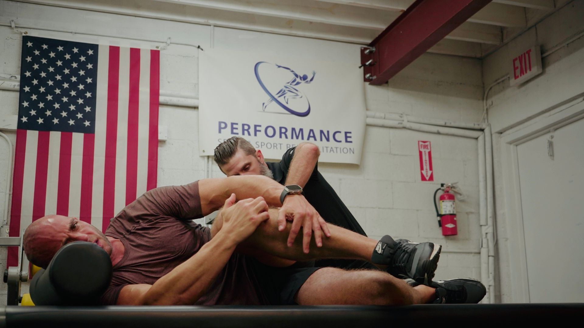 Man receiving knee treatment from another person in a gym.