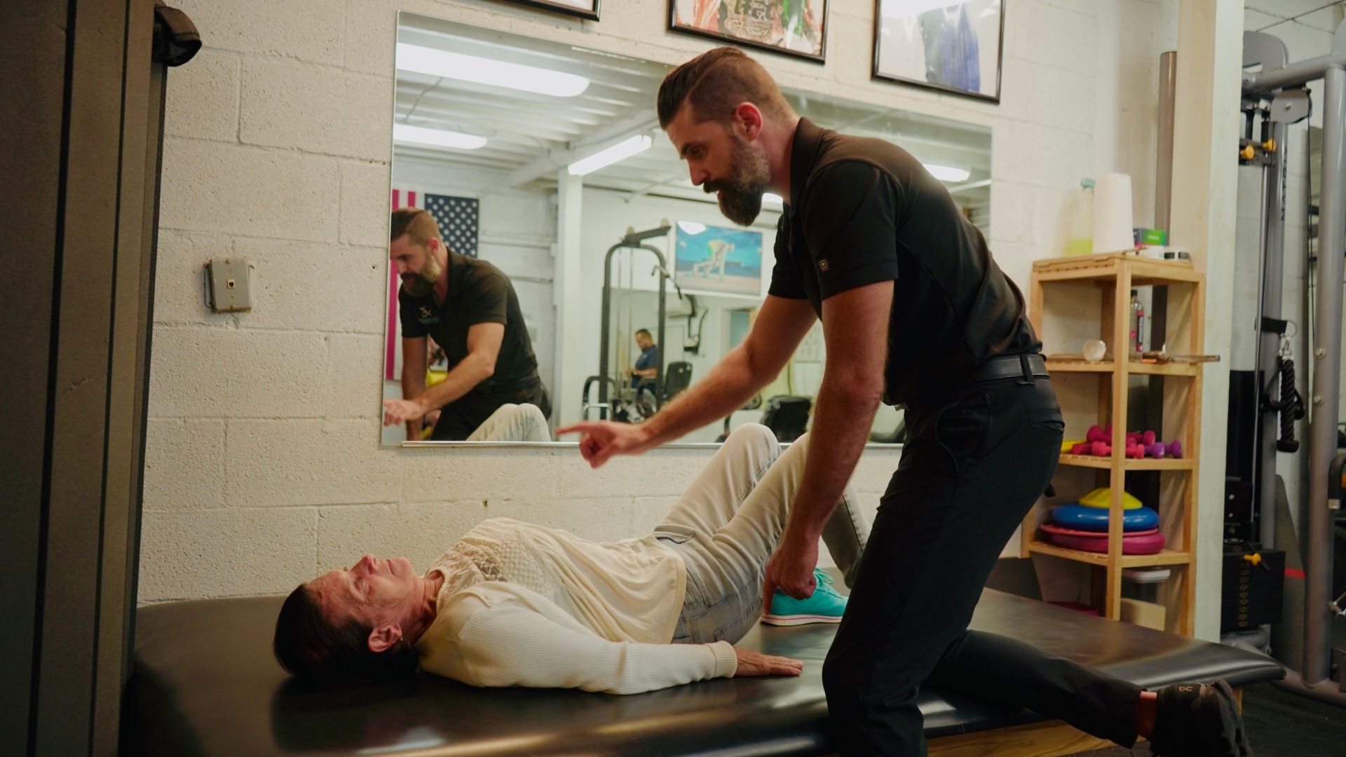 Man assisting person lying on a table in a physical therapy setting.
