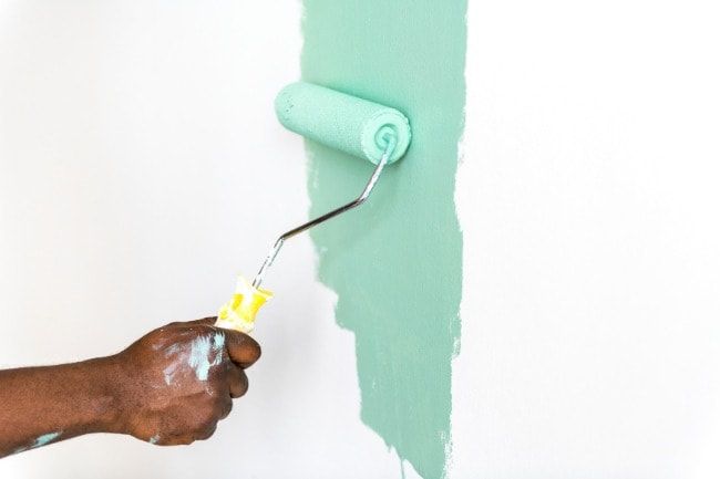 A person is painting a wall with a paint roller.