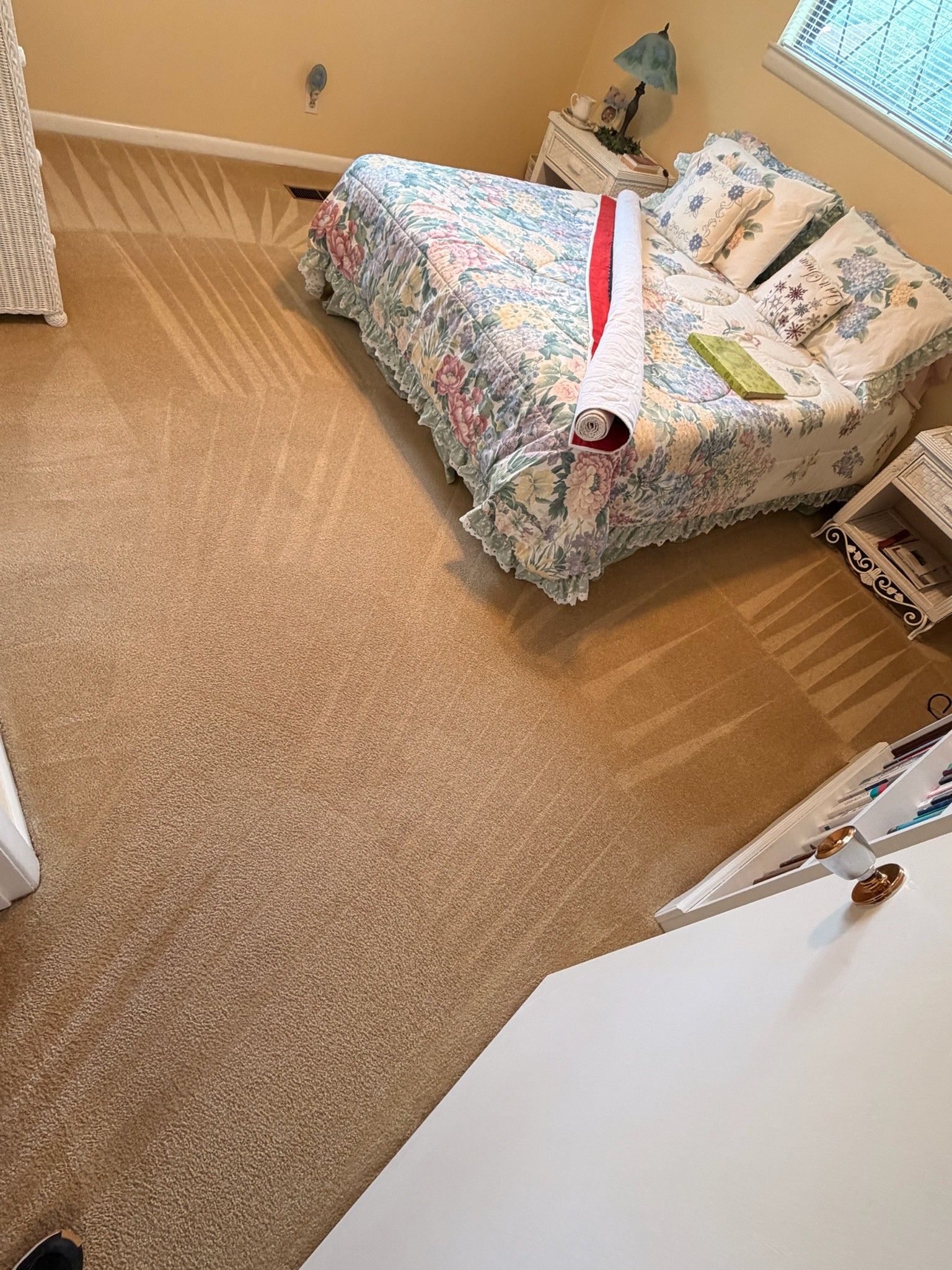 Small bedroom with a floral bedspread, beige carpet, and a white desk in the foreground.