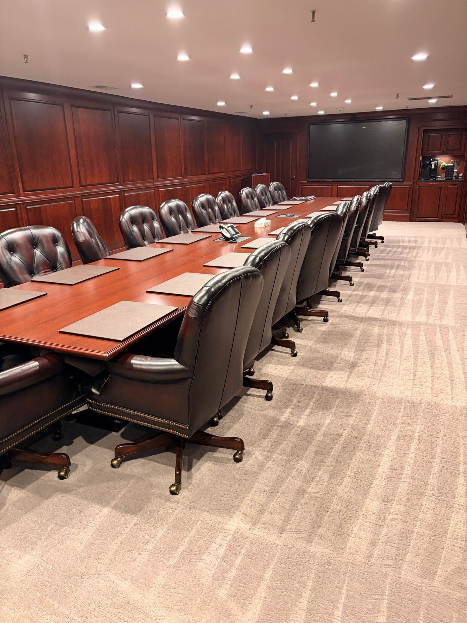 Empty wood-paneled conference room with long table, black chairs, and ceiling lights