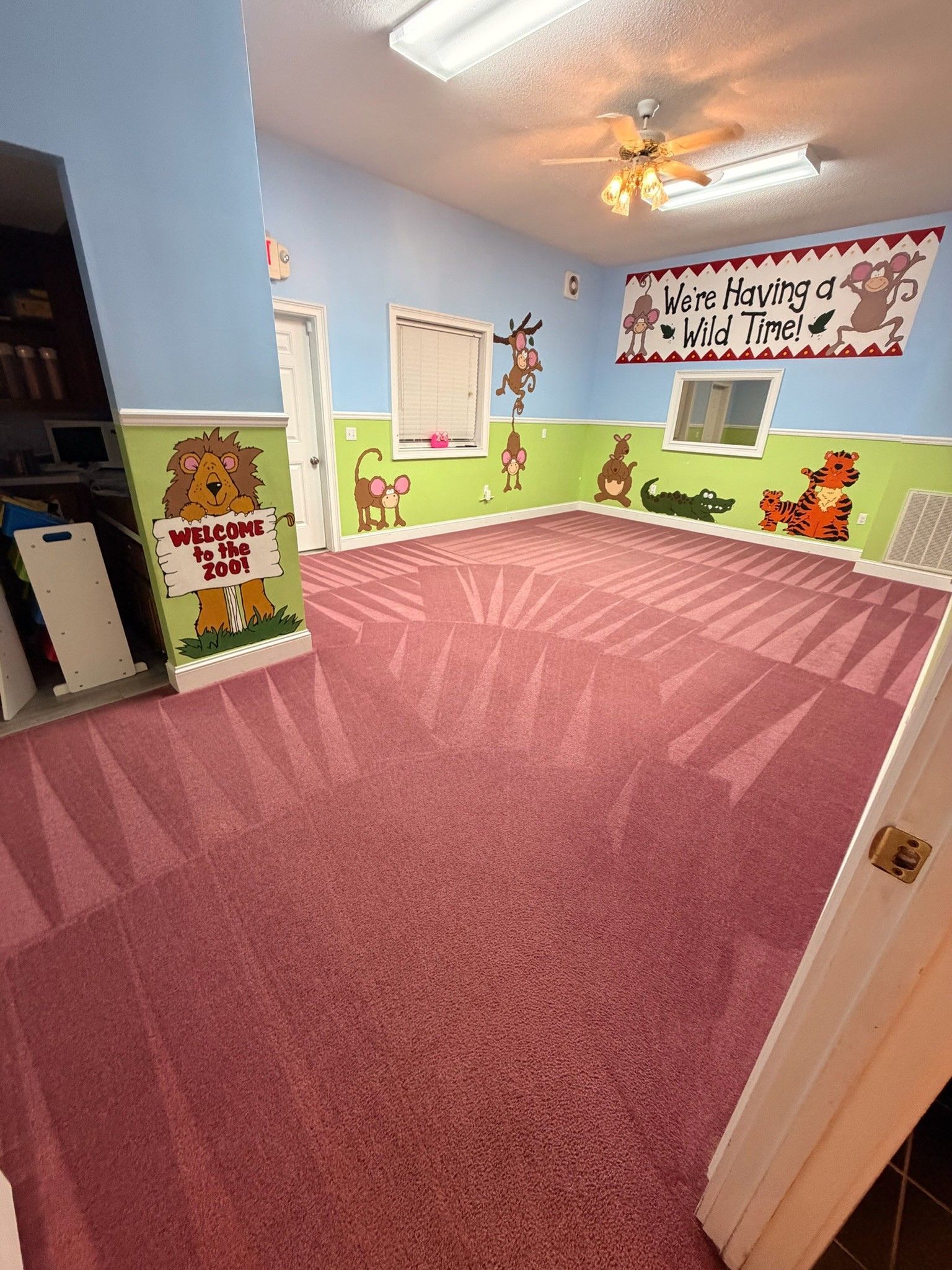 Colorful empty classroom with pink carpet, blue walls, children’s murals, and bright ceiling lights