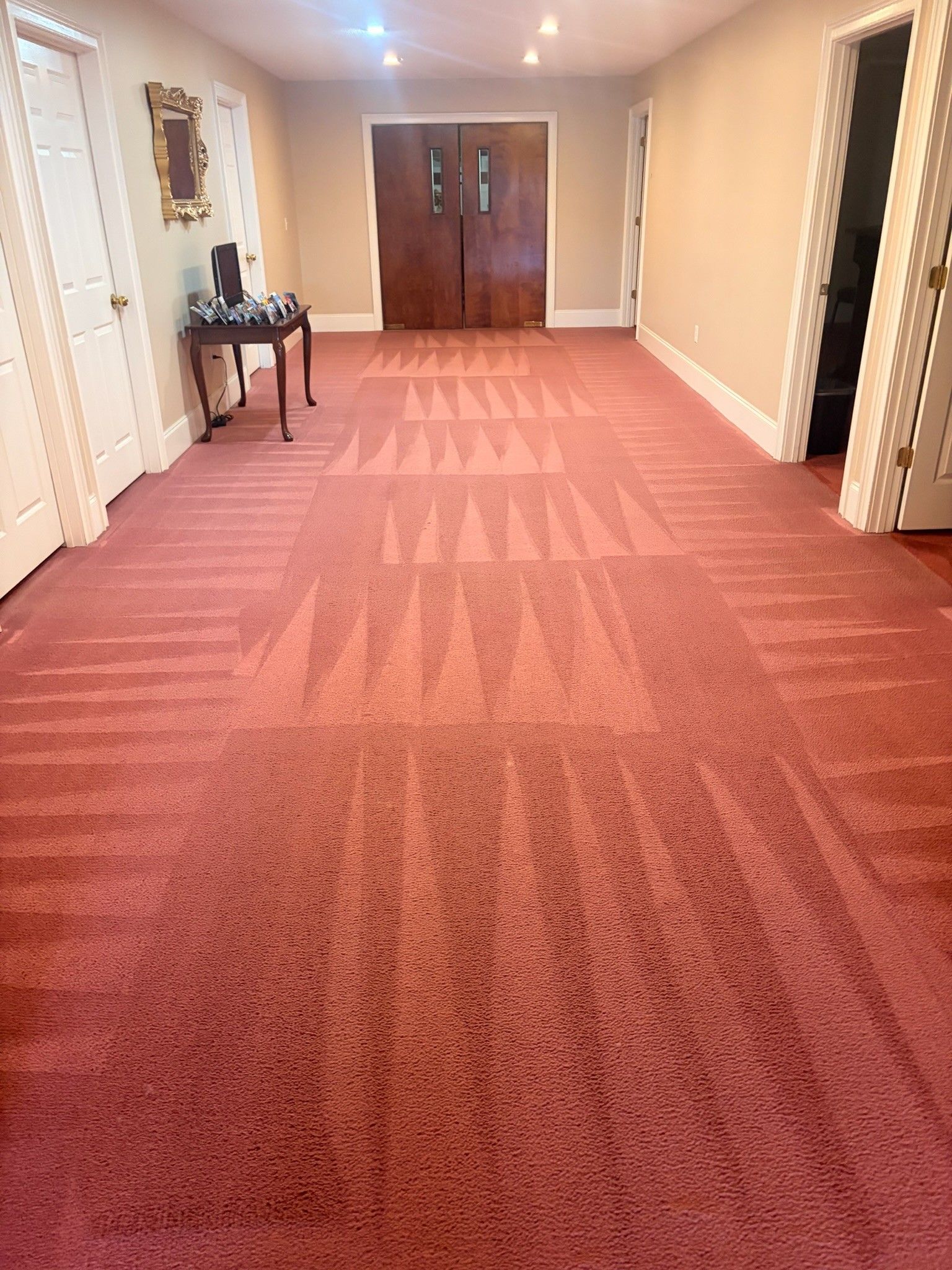 Wide hotel hallway with red carpet, cream walls, wall mirrors, and double doors at the end.