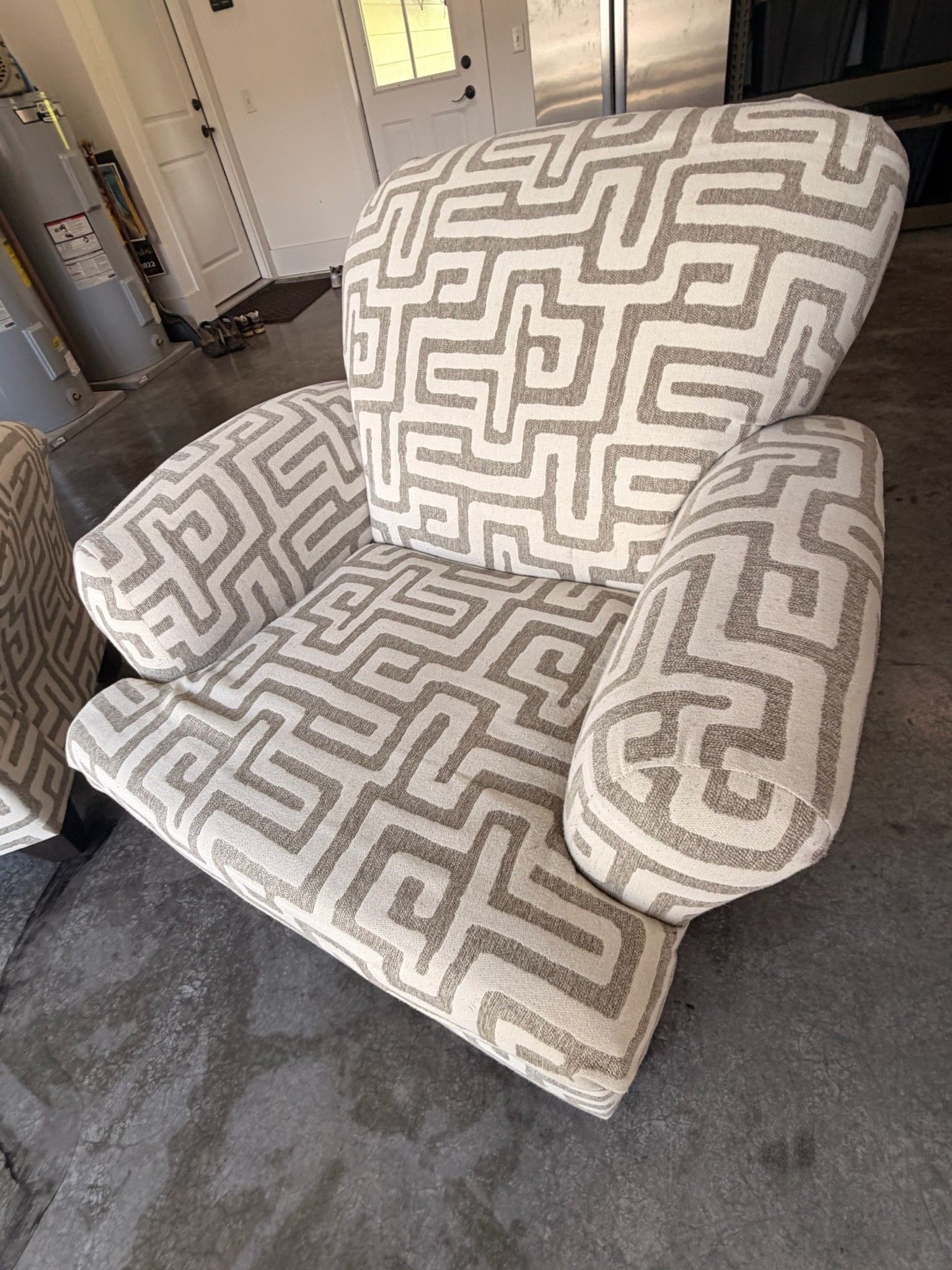 Patterned beige armchair with matching ottoman on a concrete floor indoors