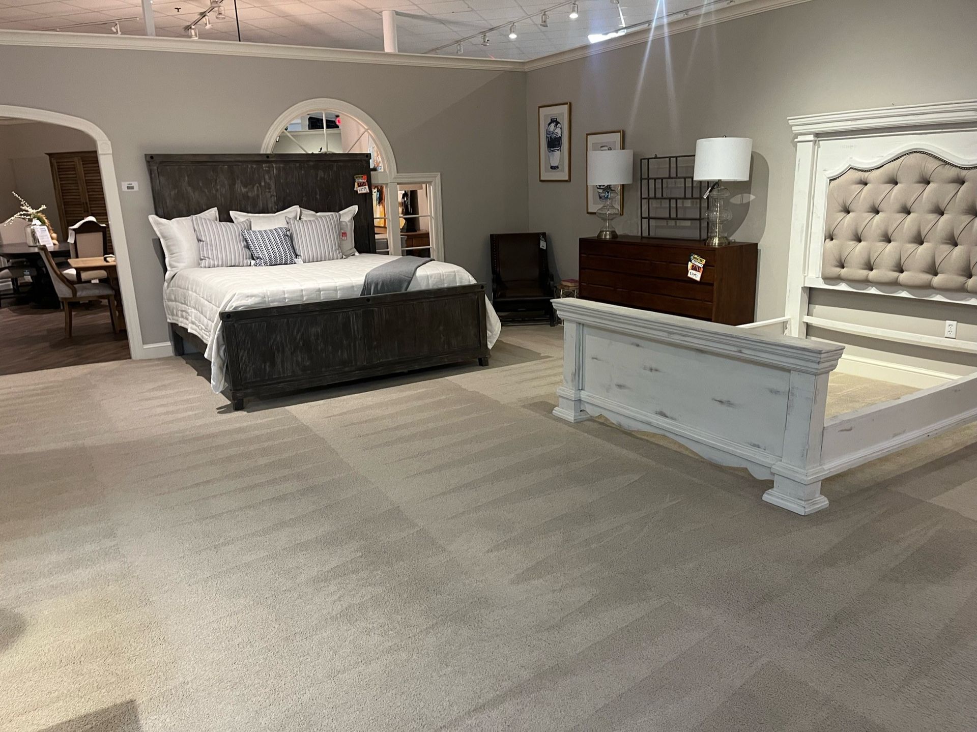 Spacious bedroom with two upholstered beds, white bench, neutral carpet, and soft gray walls