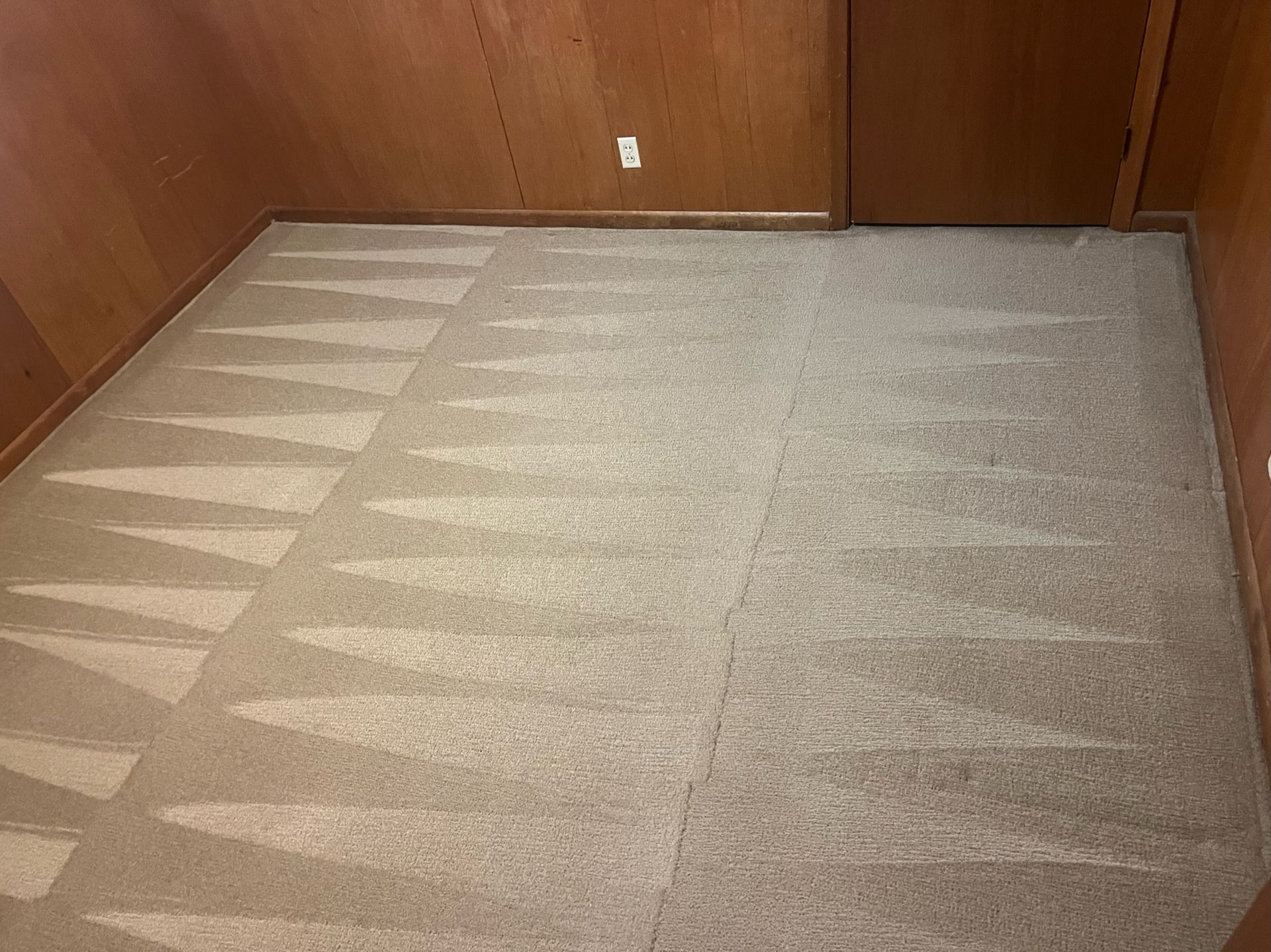 Empty carpeted room with wood-paneled walls and sunlight casting striped shadows on the floor