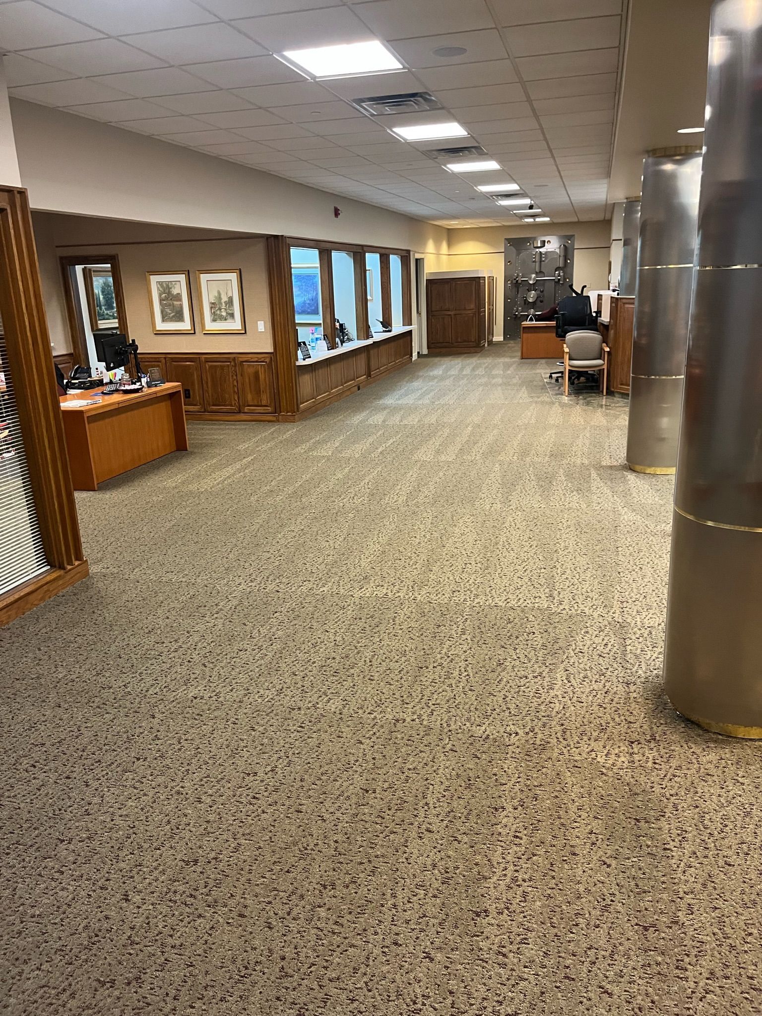Empty indoor hallway with carpet, wood paneling, framed art, and windows along the left wall.