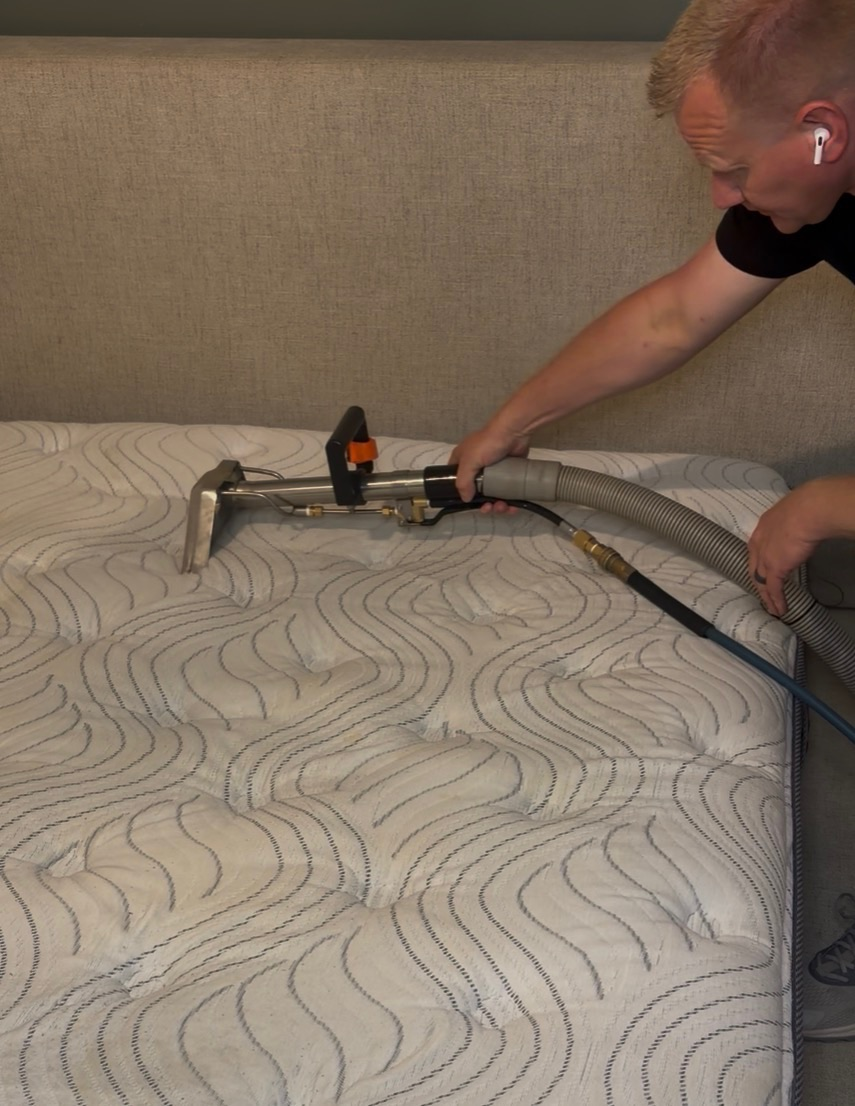 Person cleaning a mattress with a vacuum hose and attachment