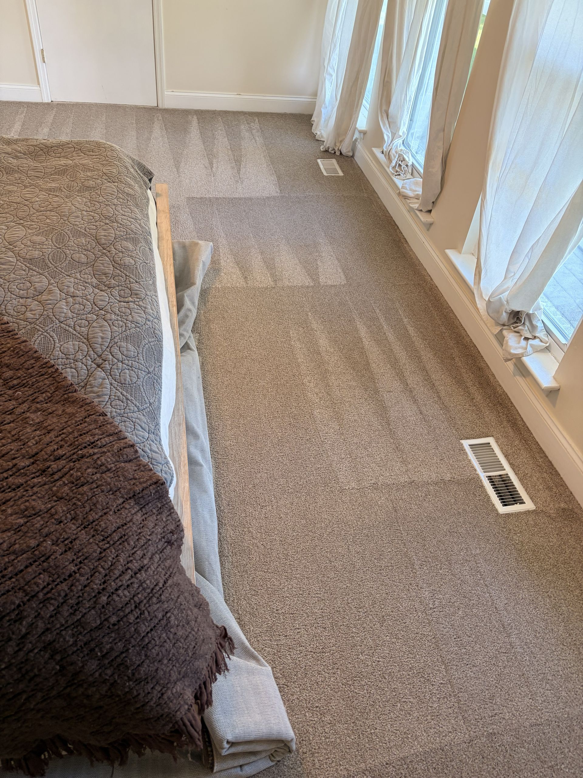 Carpeted living room floor with a long seam repair running beside a bed or couch and a window vent.