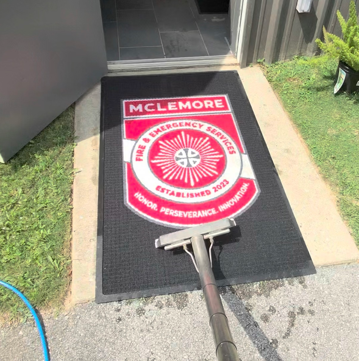 Red McLemore school mat being cleaned with a pressure washer at an outdoor doorway