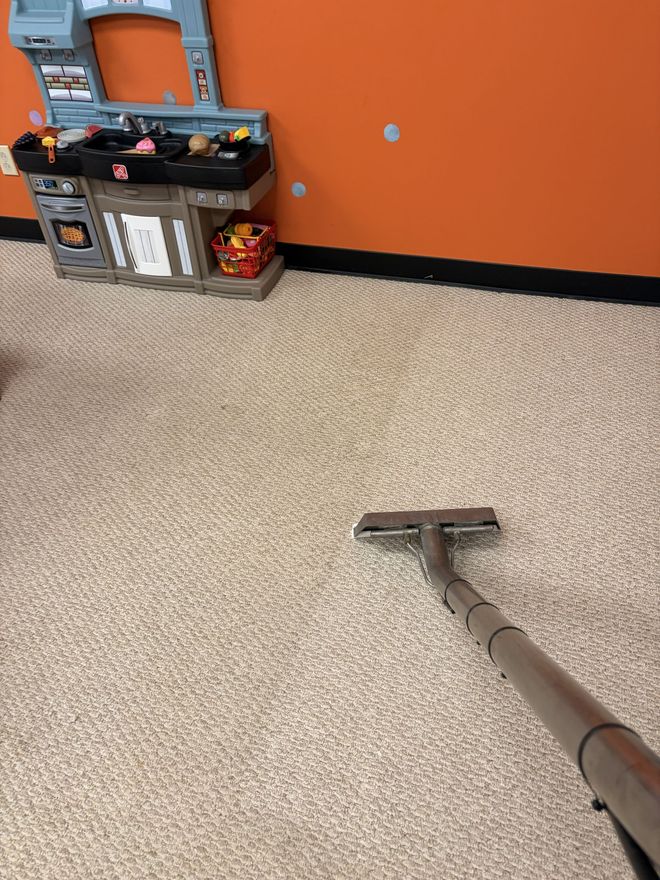 Person vacuuming a beige RV interior with sofa, kitchen, and bunk beds visible