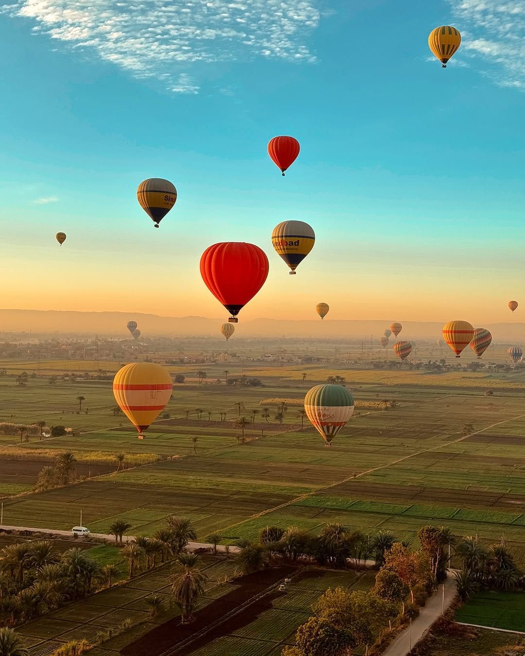 Hot air balloon flying above the green fields of Luxor