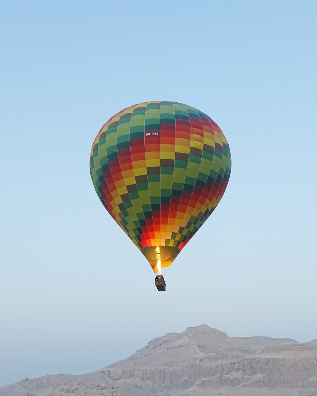 Hot air balloon flying above the green fields of Luxor