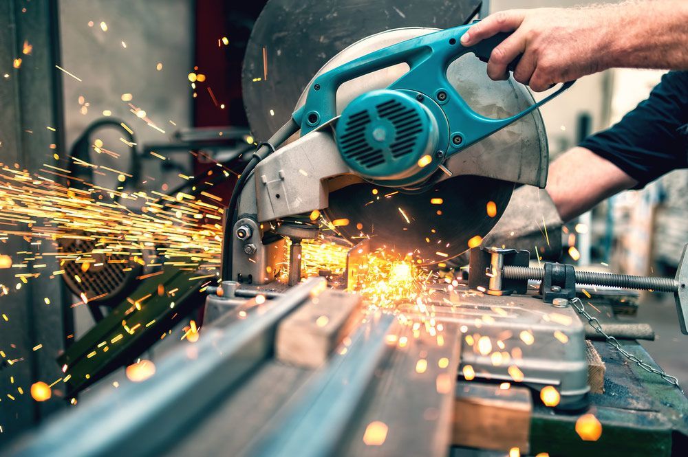 A Man Is Cutting A Piece Of Metal With A Circular Saw — Wallers Precision Tooling In Proserpine, QLD