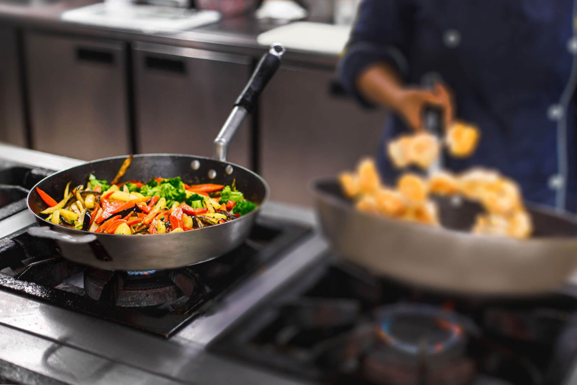 Um chef está cozinhando vegetais em uma frigideira no fogão.